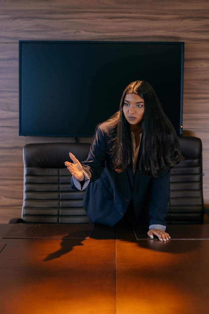 A professional woman stands assertively in a conference room, engaging in a discussion.